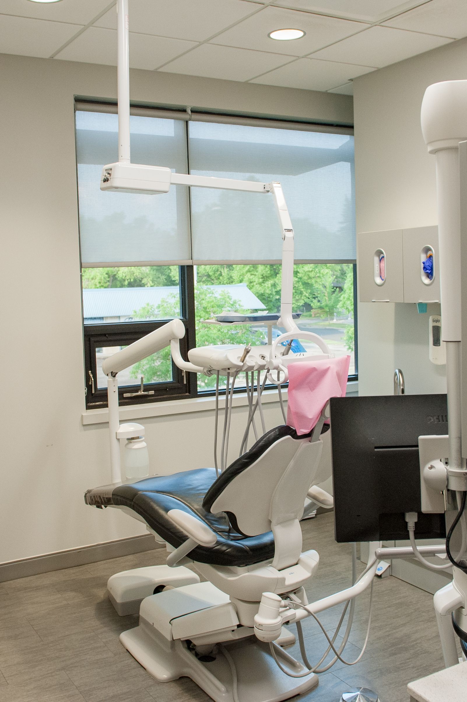 Dental chair in a bright room with window. Tools, equipment and a monitor are nearby.