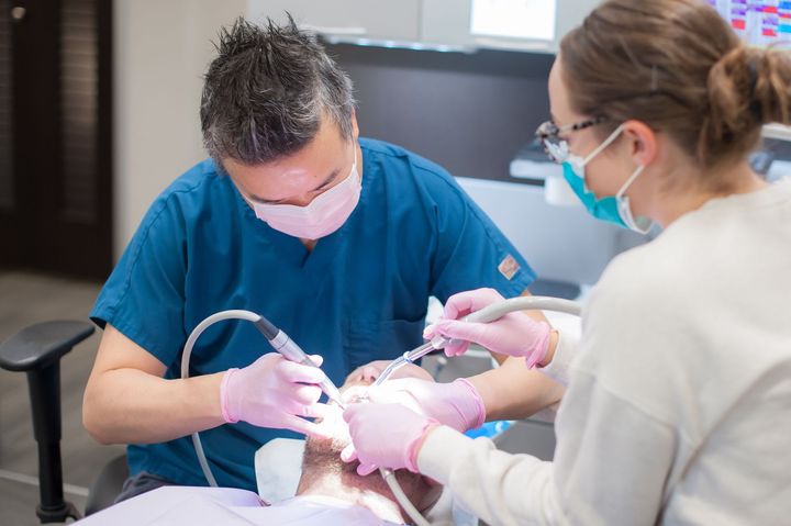 Dentist and assistant working on patient's teeth in a dental office. The dentist uses tools; the assistant helps.