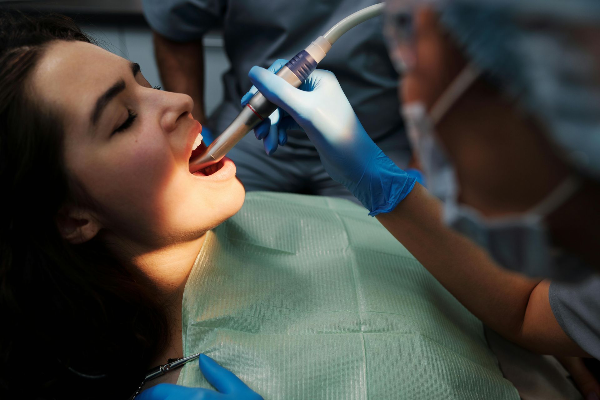 Woman receiving dental treatment, mouth open, dentist using a tool.