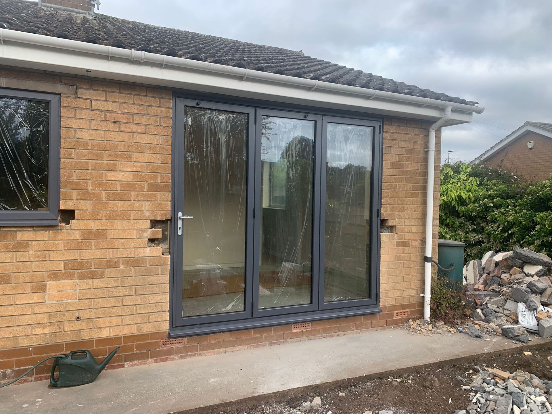 Three-panel grey-framed glass bifold door in brick. building exterior, overcast day.