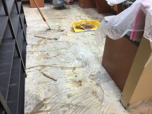 A person is cleaning a dirty floor with a broom.