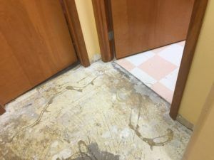 A dirty floor in a hallway next to a door.