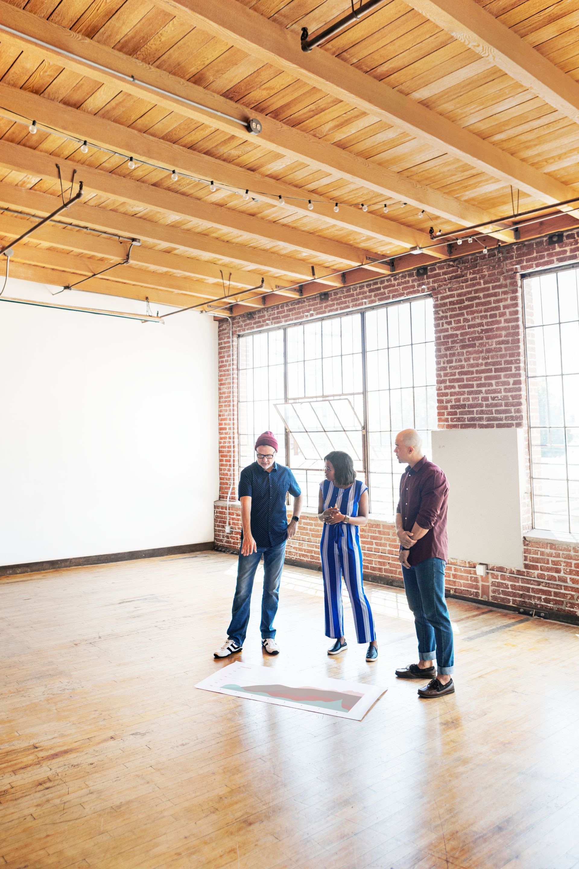 Three people are standing in an empty room with a wooden ceiling.