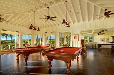 Two pool tables in a large room with ceiling fans