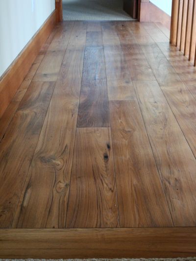 A wooden floor in a hallway with a staircase in the background