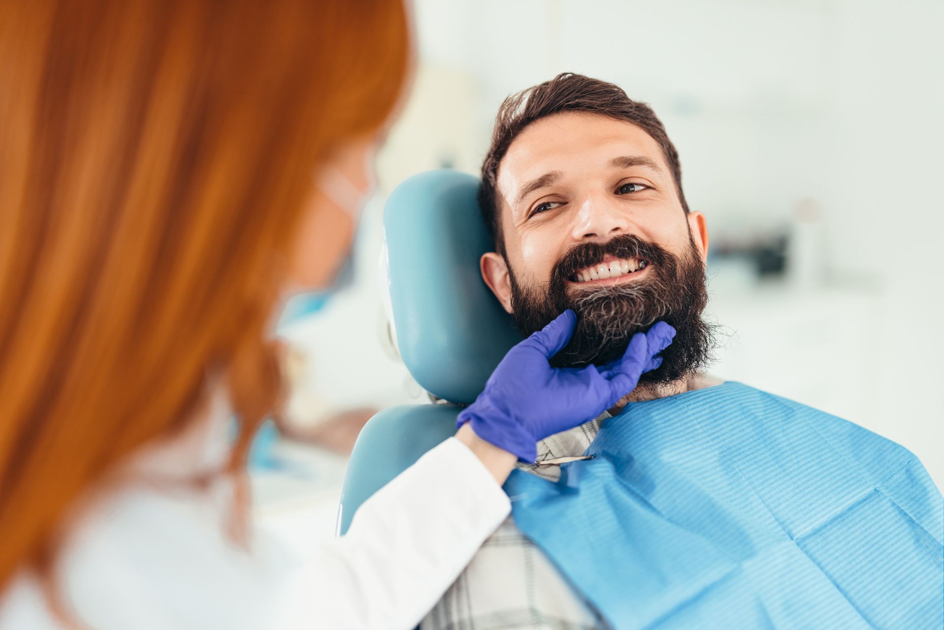 Un uomo con la barba è seduto sulla poltrona del dentista mentre un dentista gli esamina i denti.