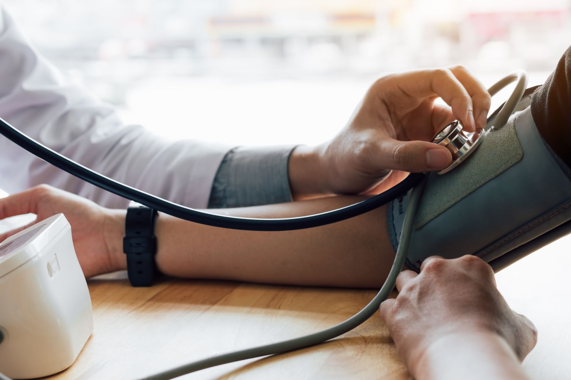 Doctor using a stethoscope to take a patient's blood pressure with an automated cuff on the arm.