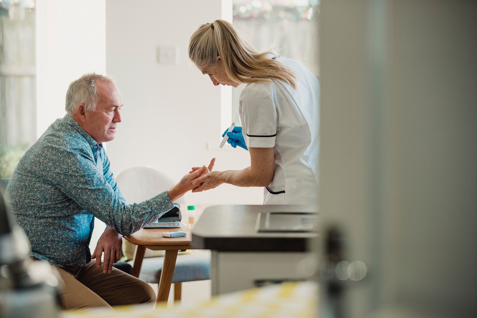 Nurse taking a blood sample from a patient's finger in a medical setting.