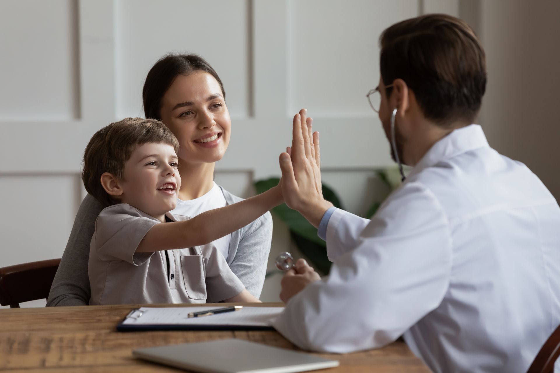 Child high-fives a doctor in an office while sitting with their mother. All are smiling.
