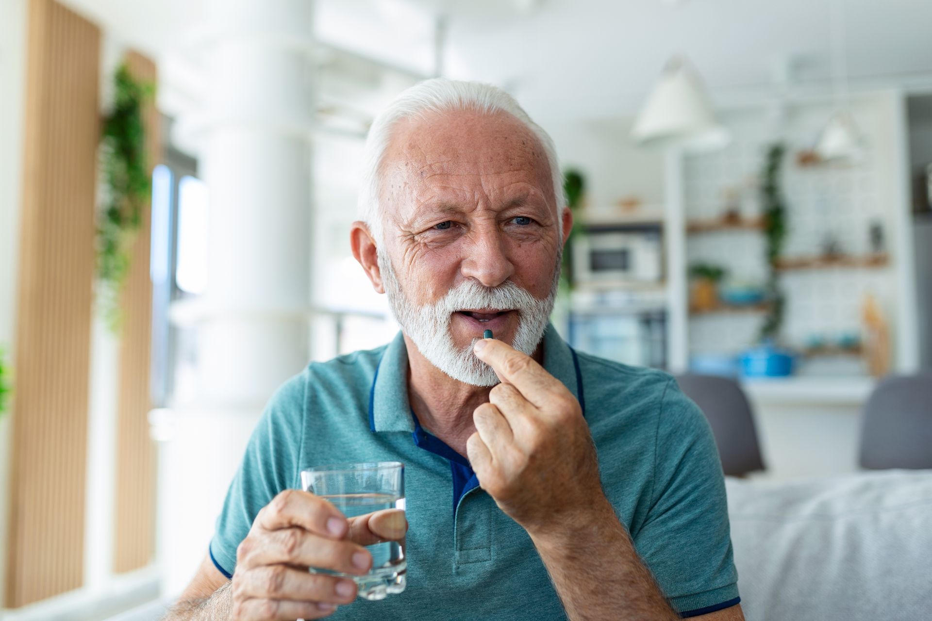 An older person holding a pill and a glass of water, about to take medication.