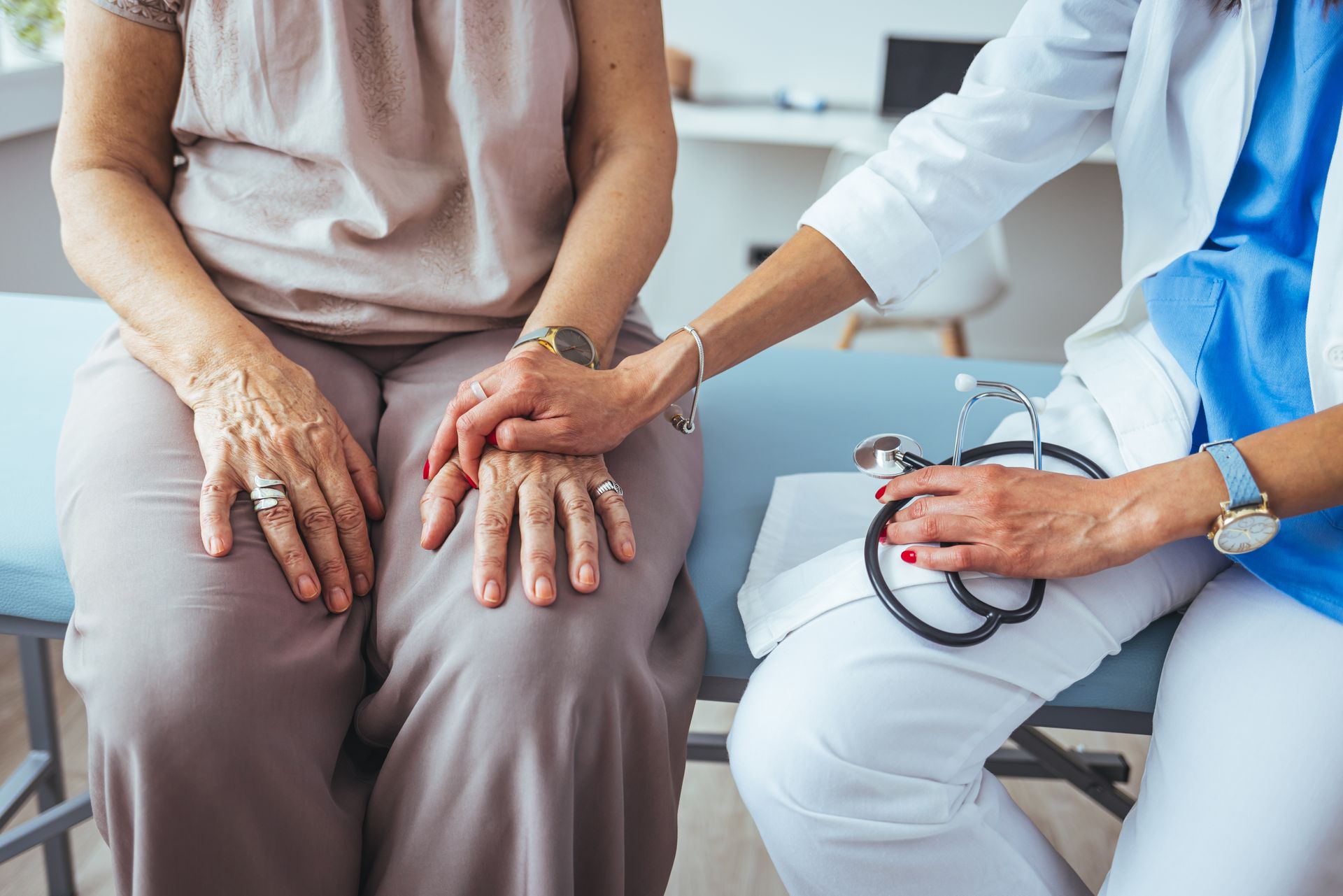 Doctor holding patient's hand for comfort, stethoscope in hand.