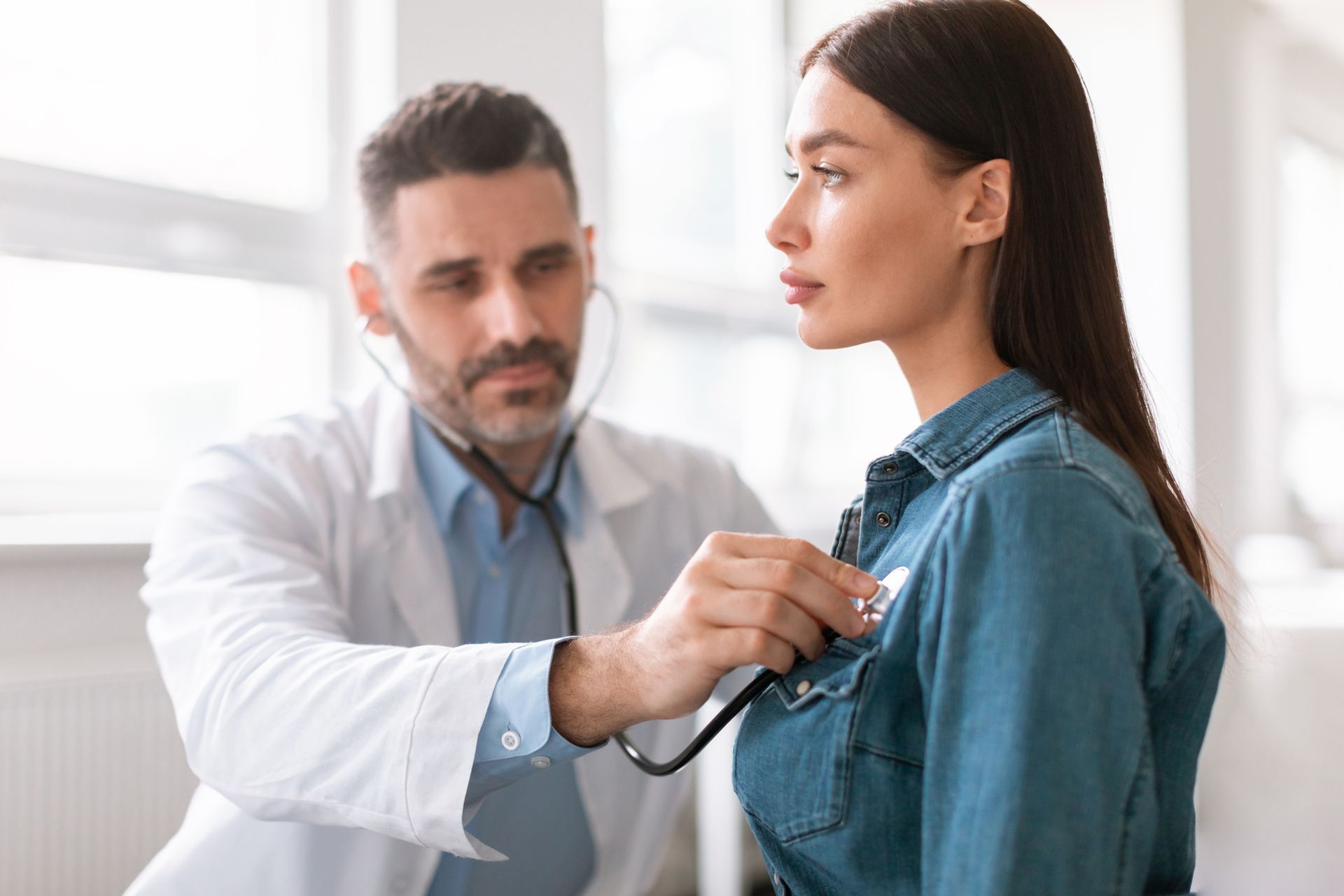 Doctor listening to a patient's chest with a stethoscope in a medical office.
