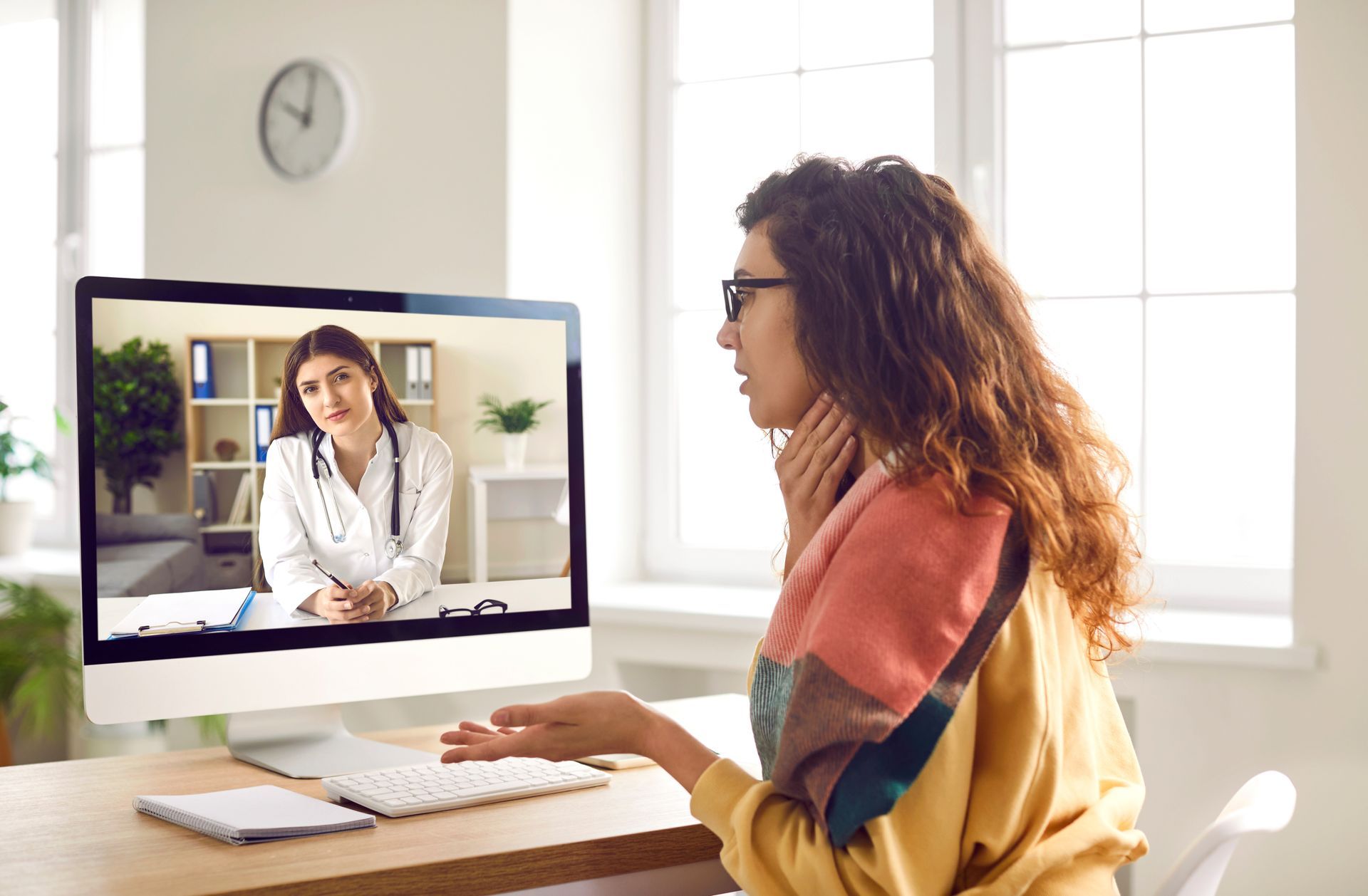 Woman having a telehealth consultation with a doctor on a computer, holding her neck.
