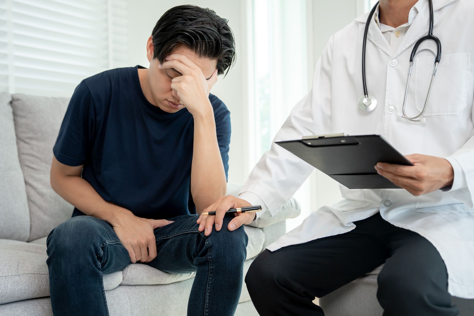 Man seated on couch with head in hand.