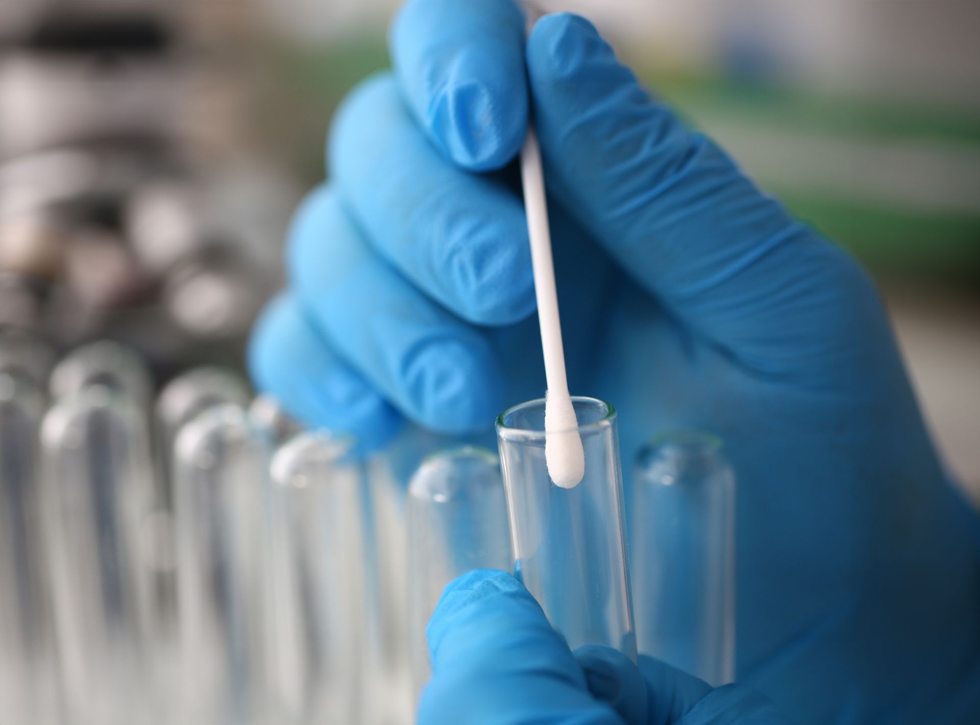 Gloved hands placing a swab into a test tube in a laboratory.