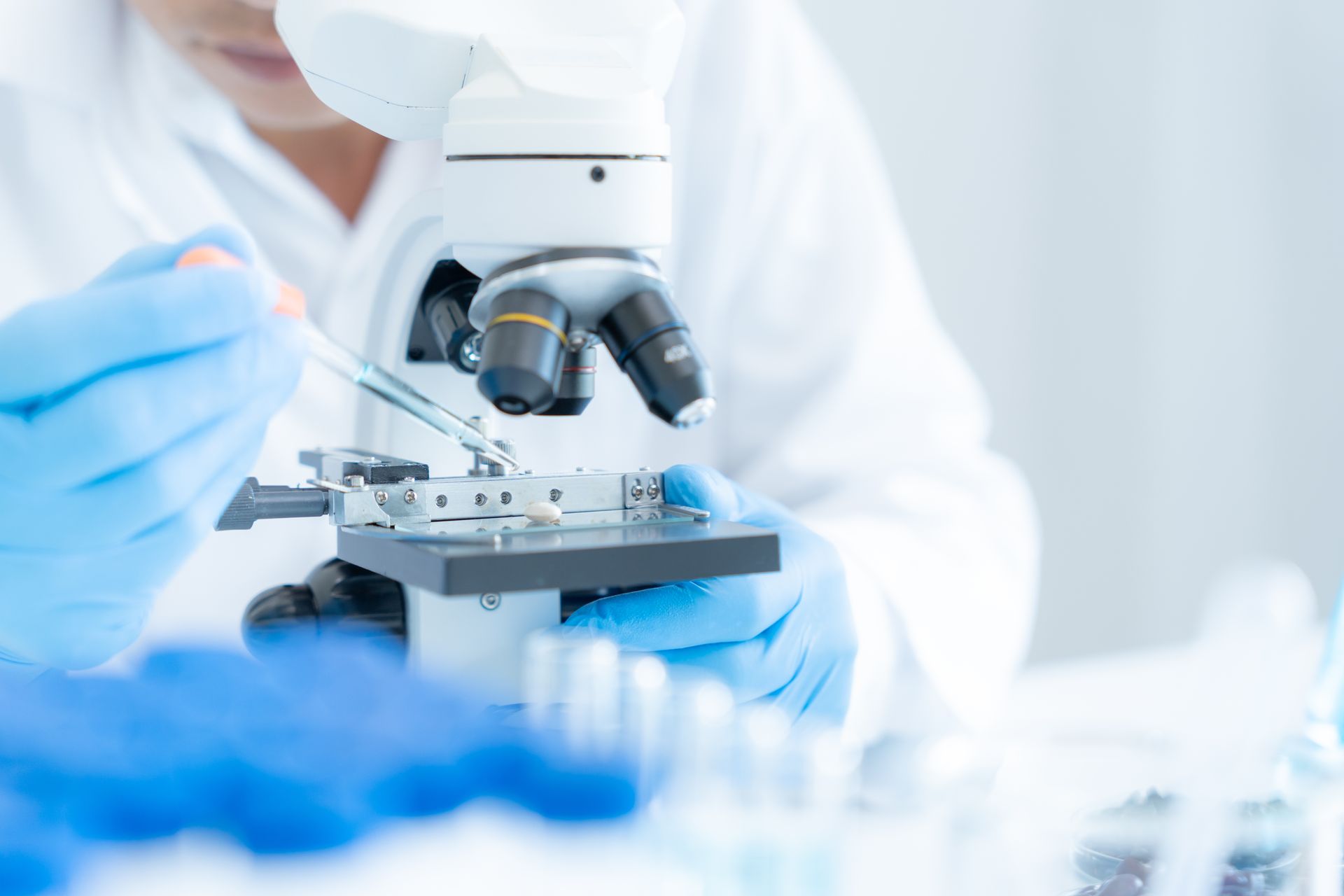 Scientist using a microscope in a laboratory, wearing blue gloves, holding a pipette.