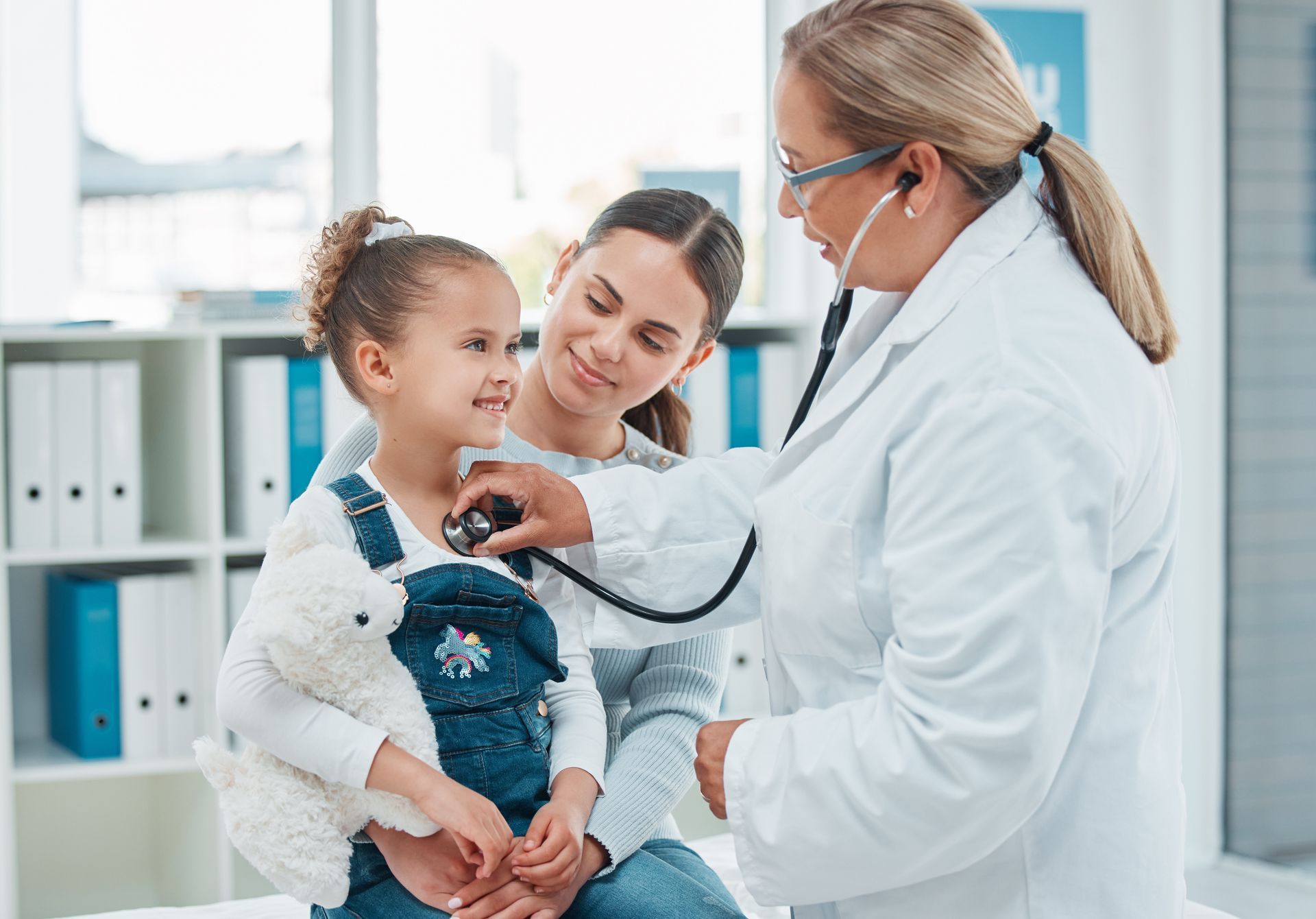 Doctor examining a young child with a stethoscope, mother present.