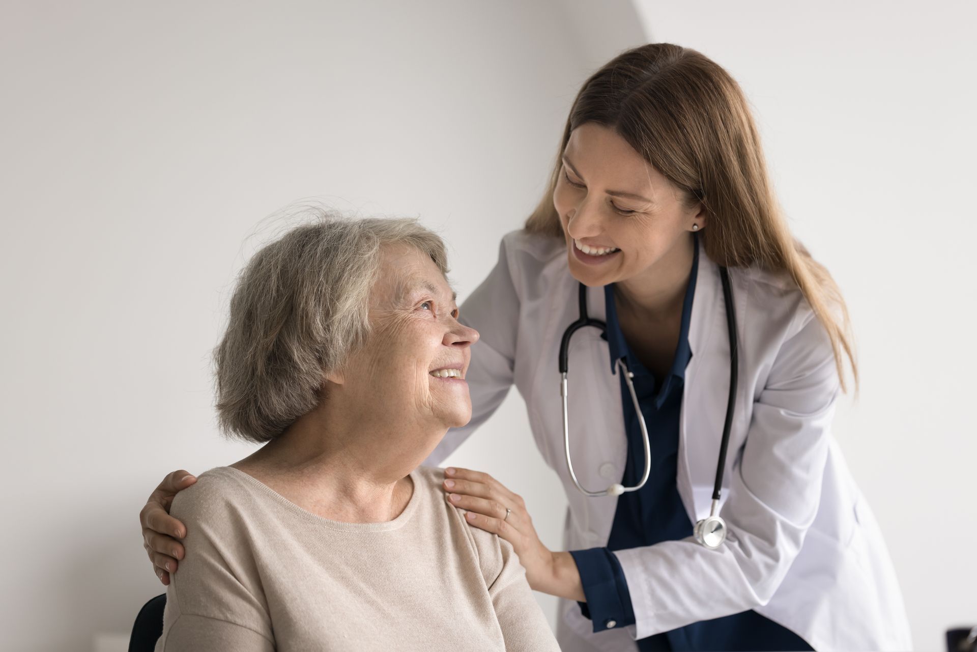 Doctor comforting elderly patient, smiling, touching shoulder in a light-filled setting.