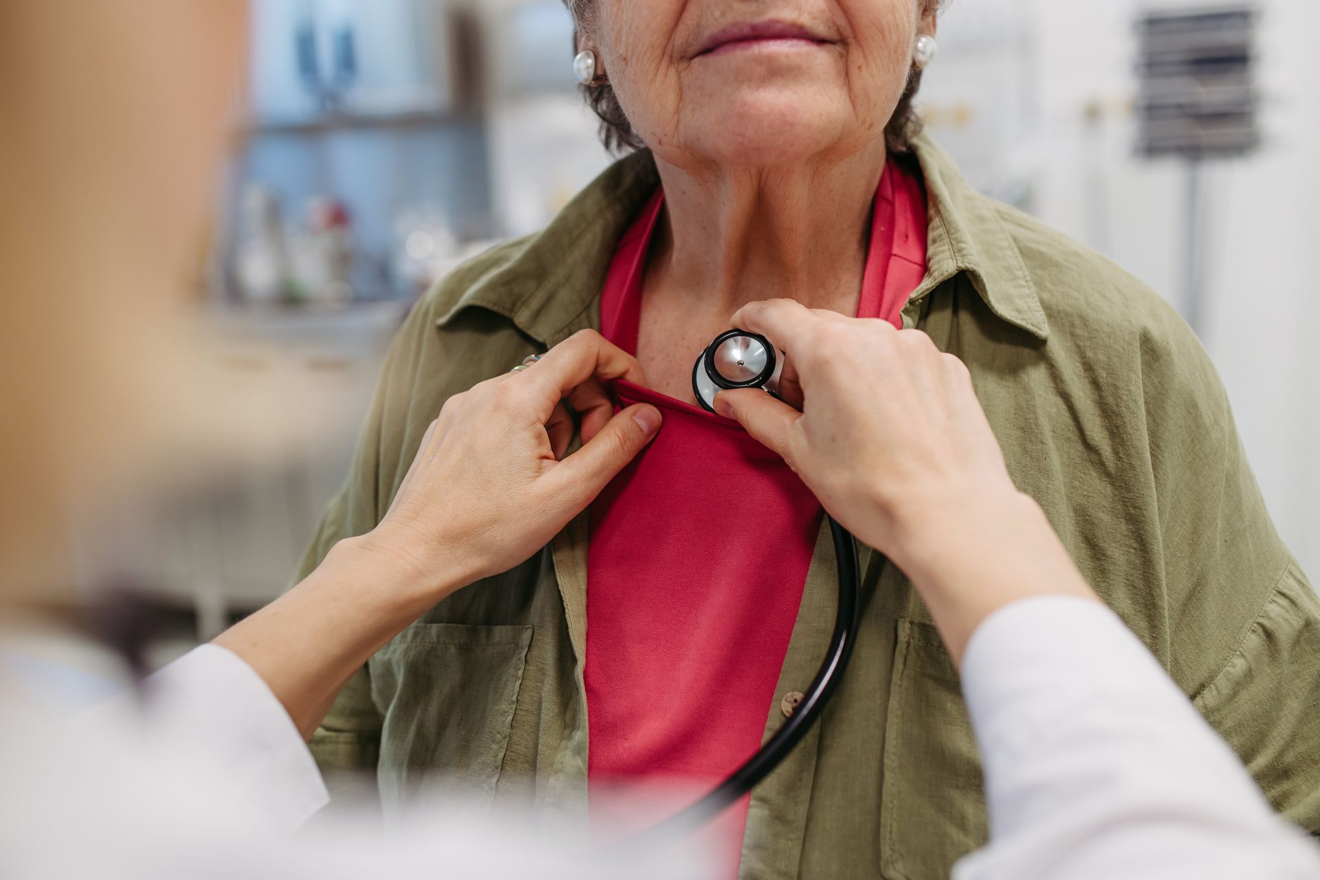 Doctor using a stethoscope to examine a patient's chest in a medical setting.