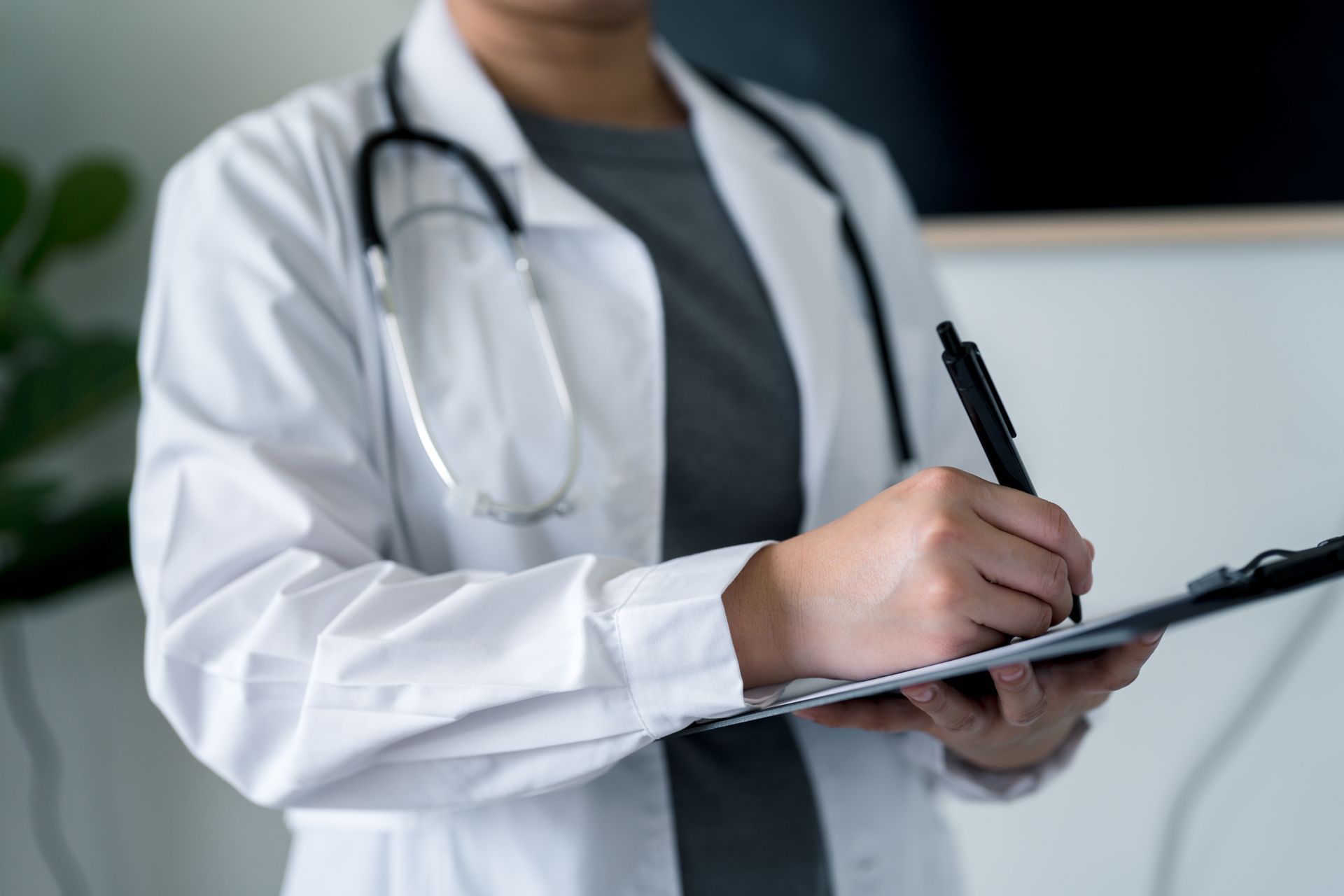 Doctor in white coat writing on a clipboard, stethoscope around neck.