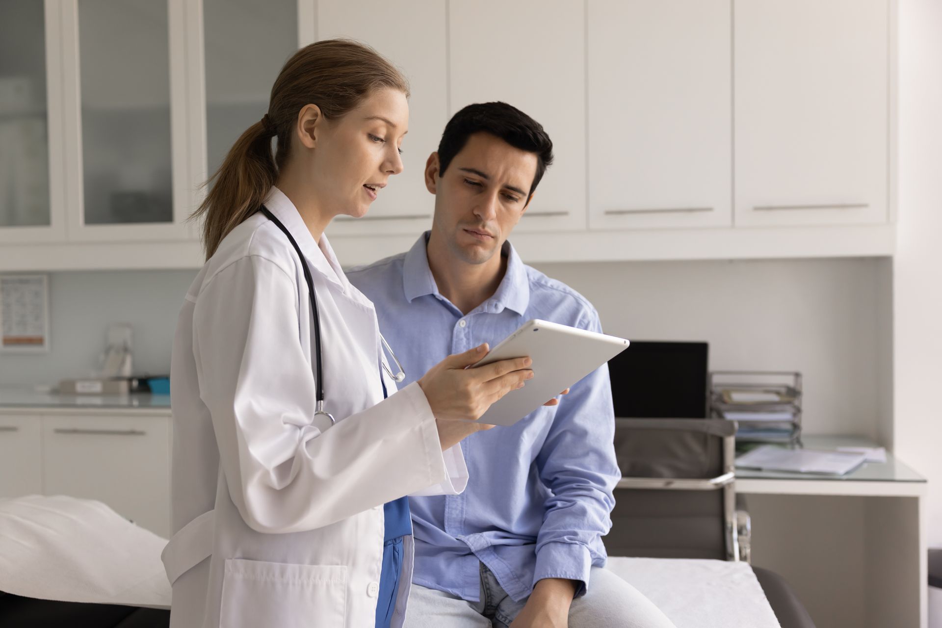 Doctor shows male patient a tablet in a medical examination room.