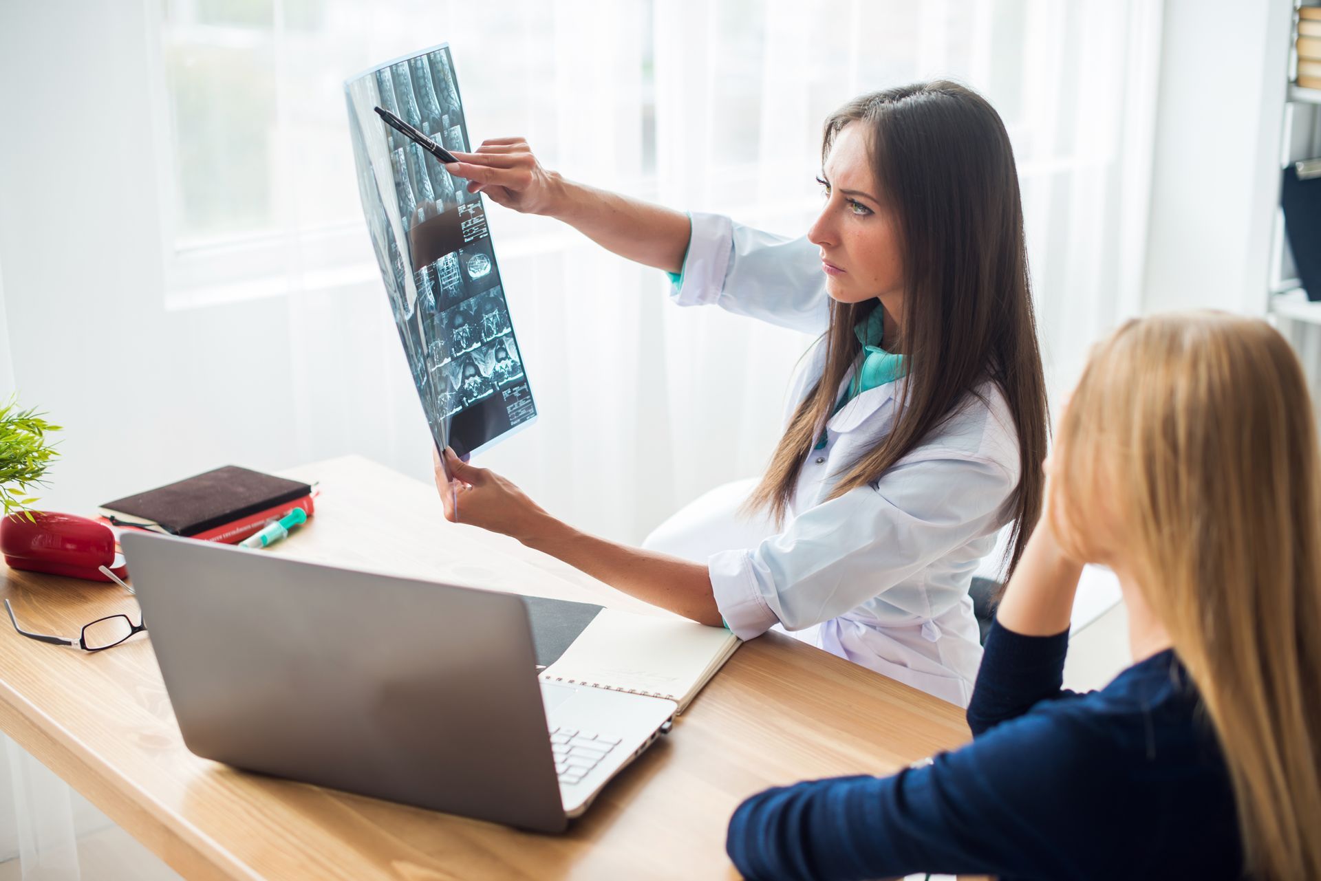 Doctor pointing at X-ray, explaining to patient at a desk.