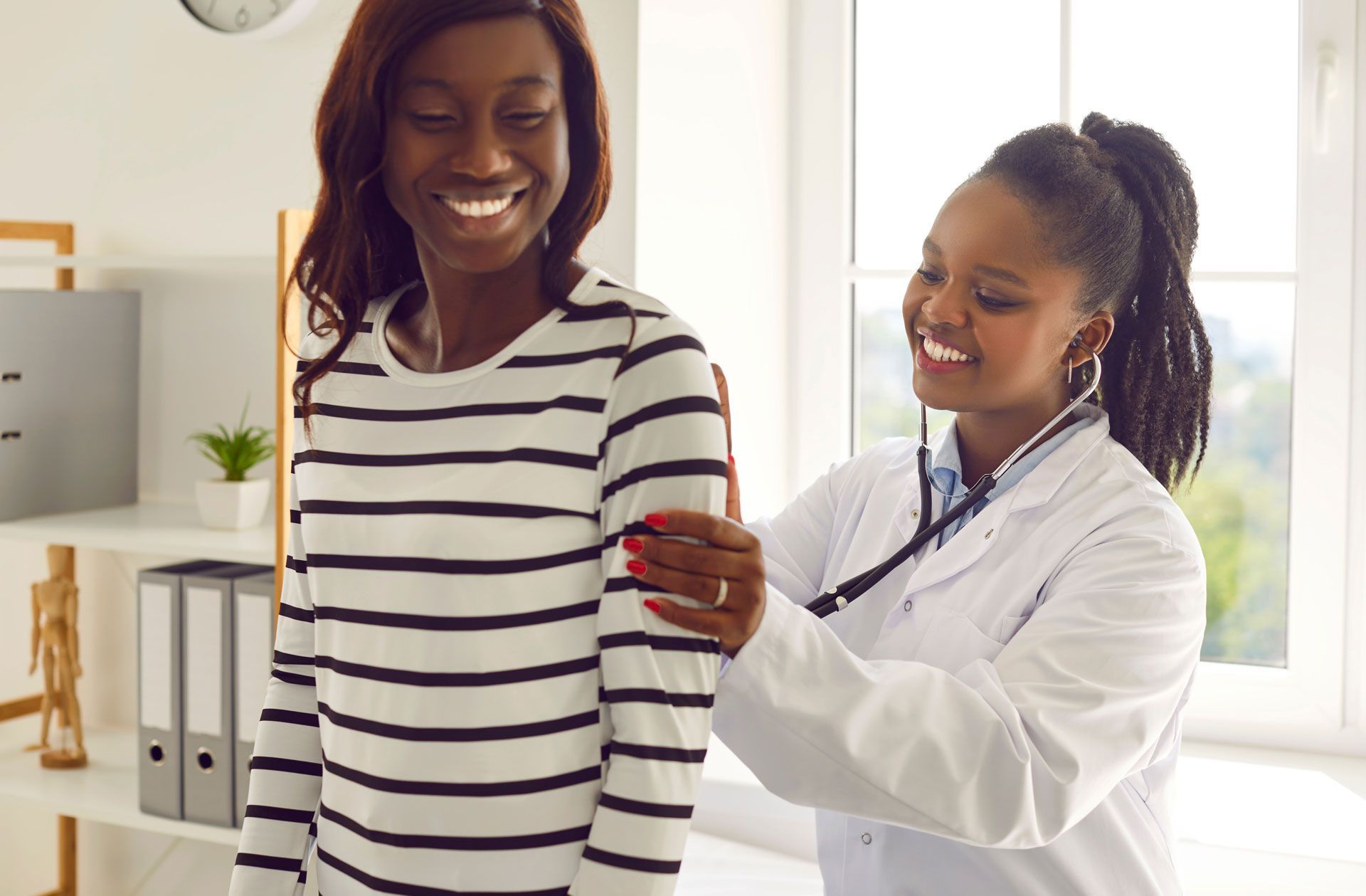 A medical professional in a white coat uses a stethoscope to examine a patient wearing a striped long-sleeve shirt.