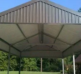 A metal carport with a roof is sitting on top of a lush green field.