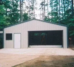 A large metal garage with a driveway and trees in the background.
