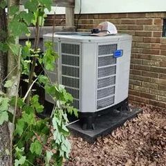 An air conditioning unit on a concrete pad next to a brick wall. A hat sits on top.