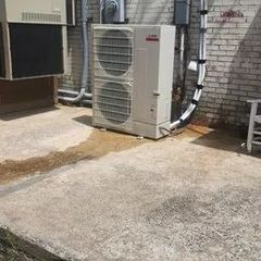 Outdoor air conditioning unit next to a brick wall on a concrete surface.