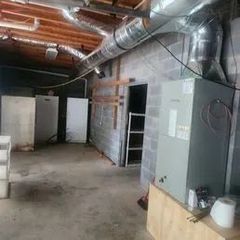 Interior of a utility room with equipment, ductwork, and a door. Concrete block walls and a concrete floor are visible.