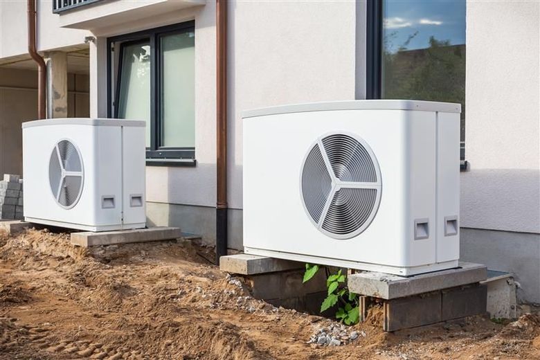 Two white heat pump units sit on concrete blocks near a building's exterior.