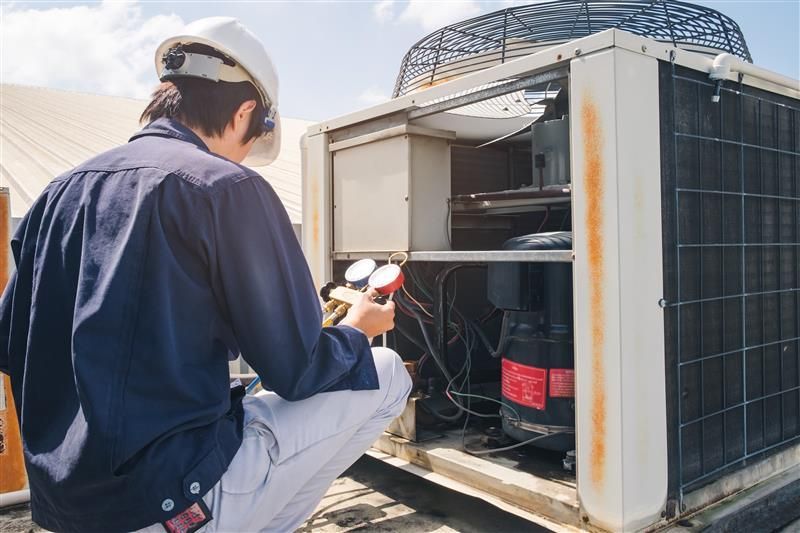 HVAC technician in a hard hat inspects rooftop air conditioning unit, using gauges.