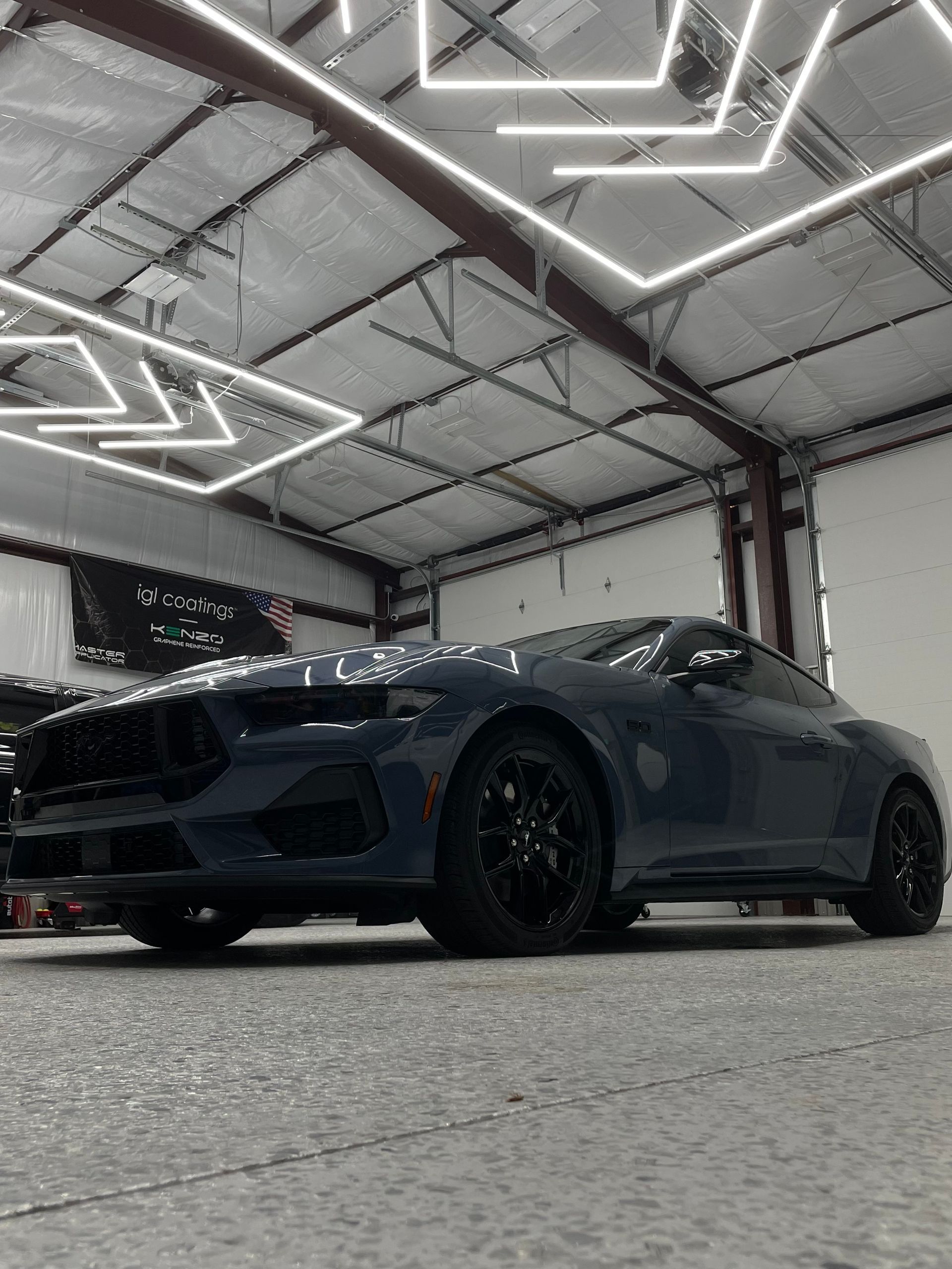 A blue car is parked in a garage with lights hanging from the ceiling.