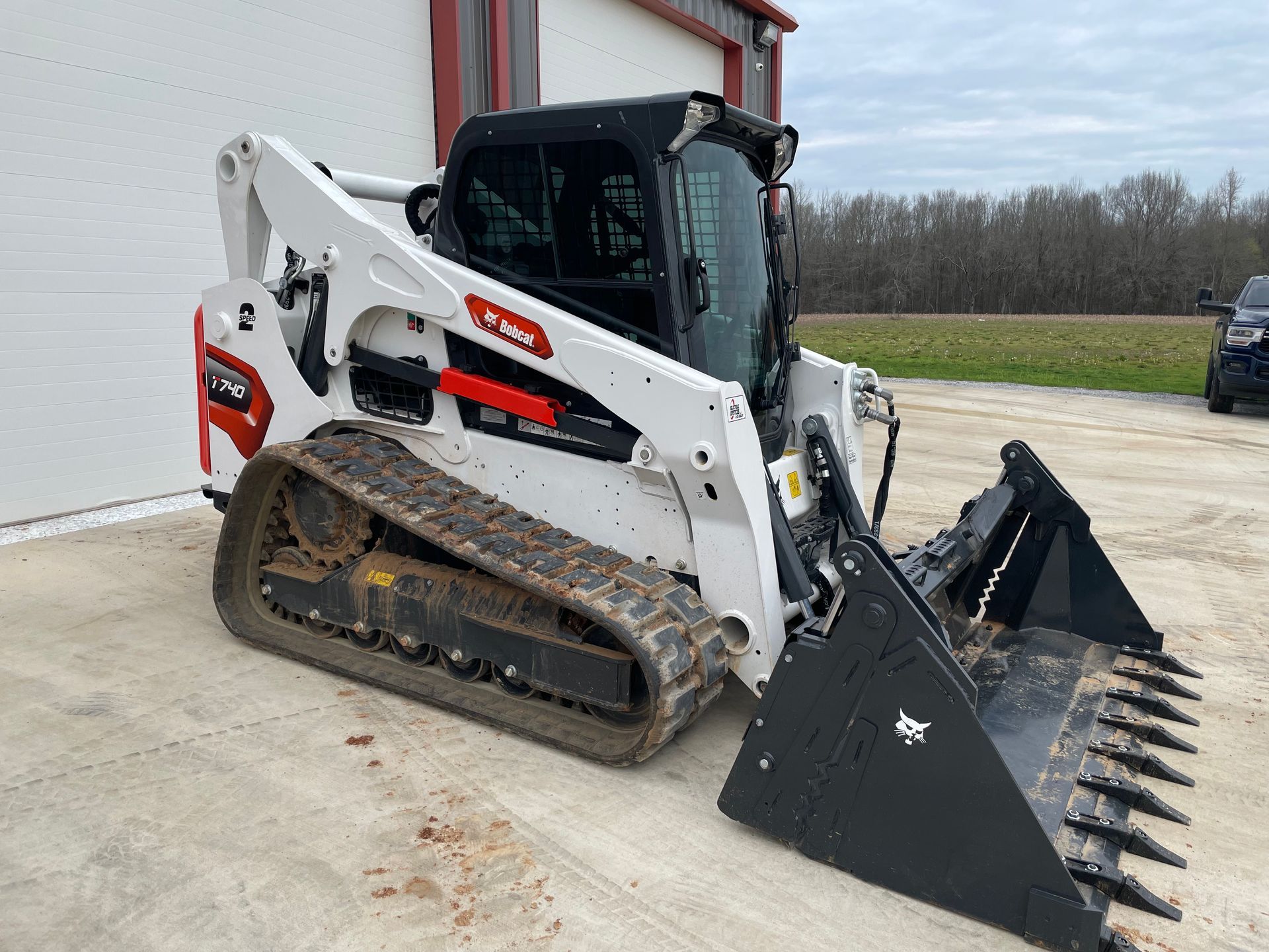 A bobcat track loader with a large bucket is parked in front of a building.