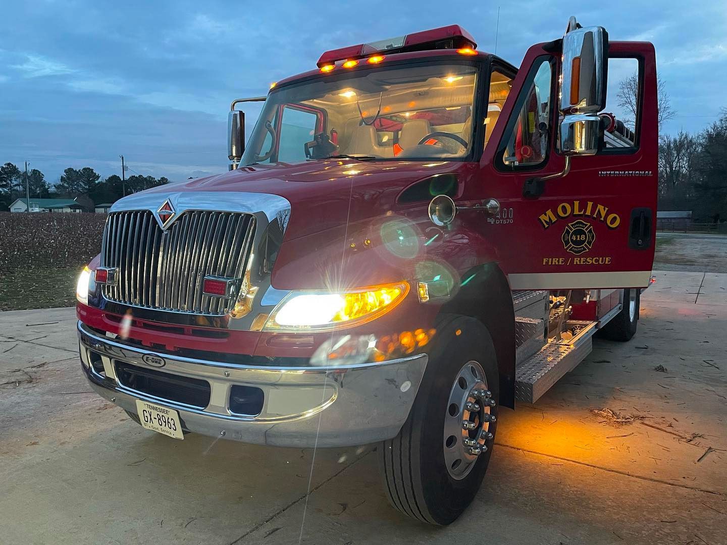 A red tow truck with the door open is parked in a parking lot.