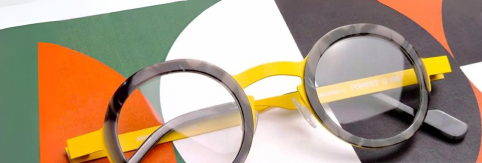 Round eyeglasses with black rims and yellow arms on a colorful, patterned surface.