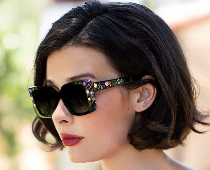 Woman with bob, sunglasses, and red lipstick outdoors; blurred background.