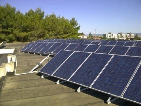 Pannelli solari installati su un tetto piano contro un cielo azzurro, con alberi ed edifici sullo sfondo.