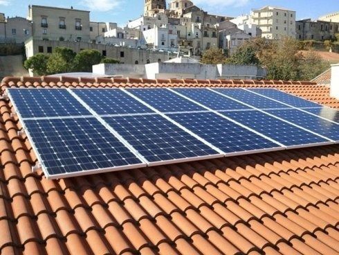 Pannelli solari su un tetto di tegole di terracotta con edifici bianchi sullo sfondo.