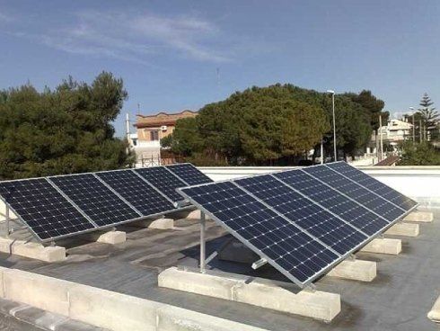 Pannelli solari installati su un tetto, orientati verso il sole. Sullo sfondo alberi verdi ed edifici.