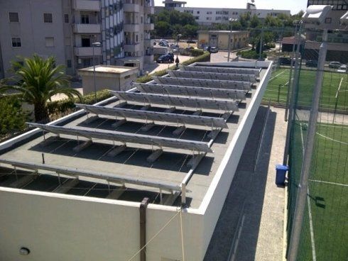 Pannelli solari su un tetto piano. Sullo sfondo si vedono edifici residenziali e un campo sportivo.