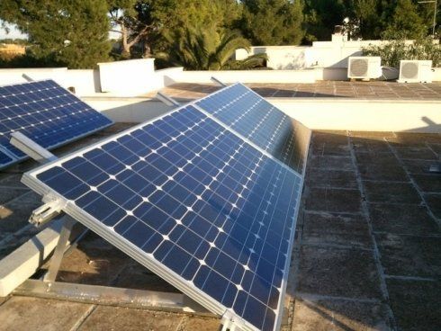 Pannelli solari su un tetto piatto, orientati verso il sole, con un edificio bianco sullo sfondo.