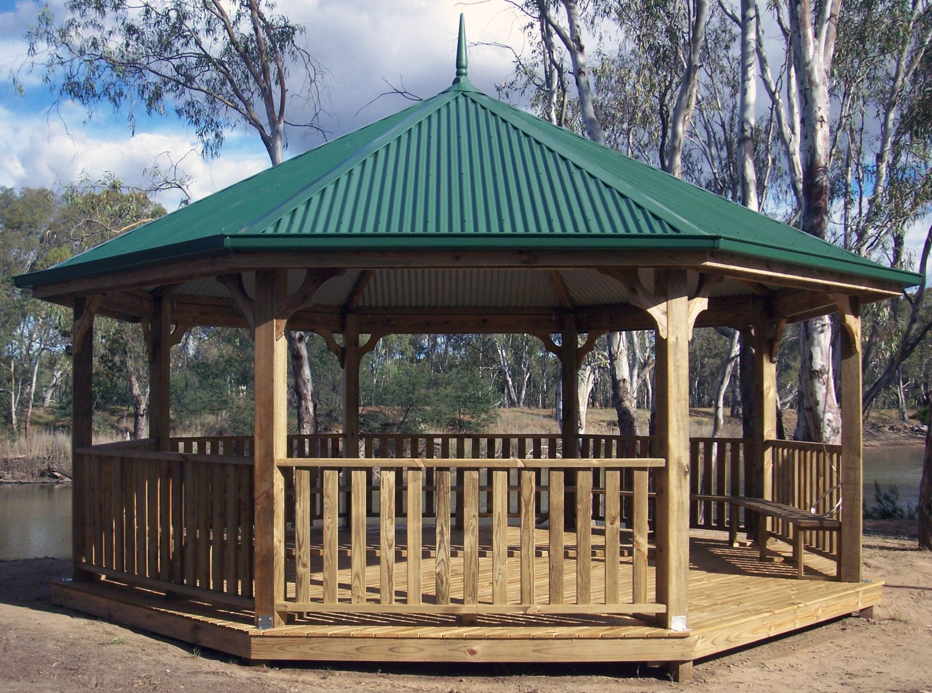 An octagonal wooden gazebo with a green corrugated metal roof, set in an outdoor area with trees and a river — The Gazebo and Shade Centre in Jindera, NSW