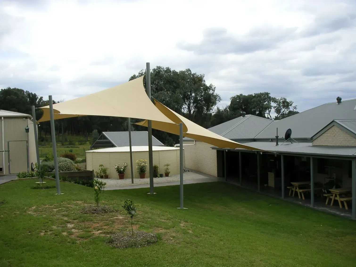 A Tan Shade Sail Structure Stretched Over a Grassy Yard — The Gazebo and Shade Centre in Jindera, NSW
