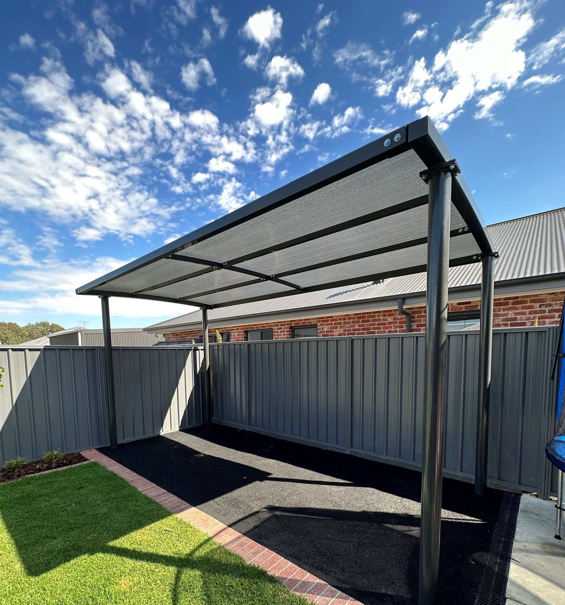 Covered backyard patio with metal roof, corrugated fence, and green lawn under a blue sky — The Gazebo and Shade Centre in Corowa, NSW