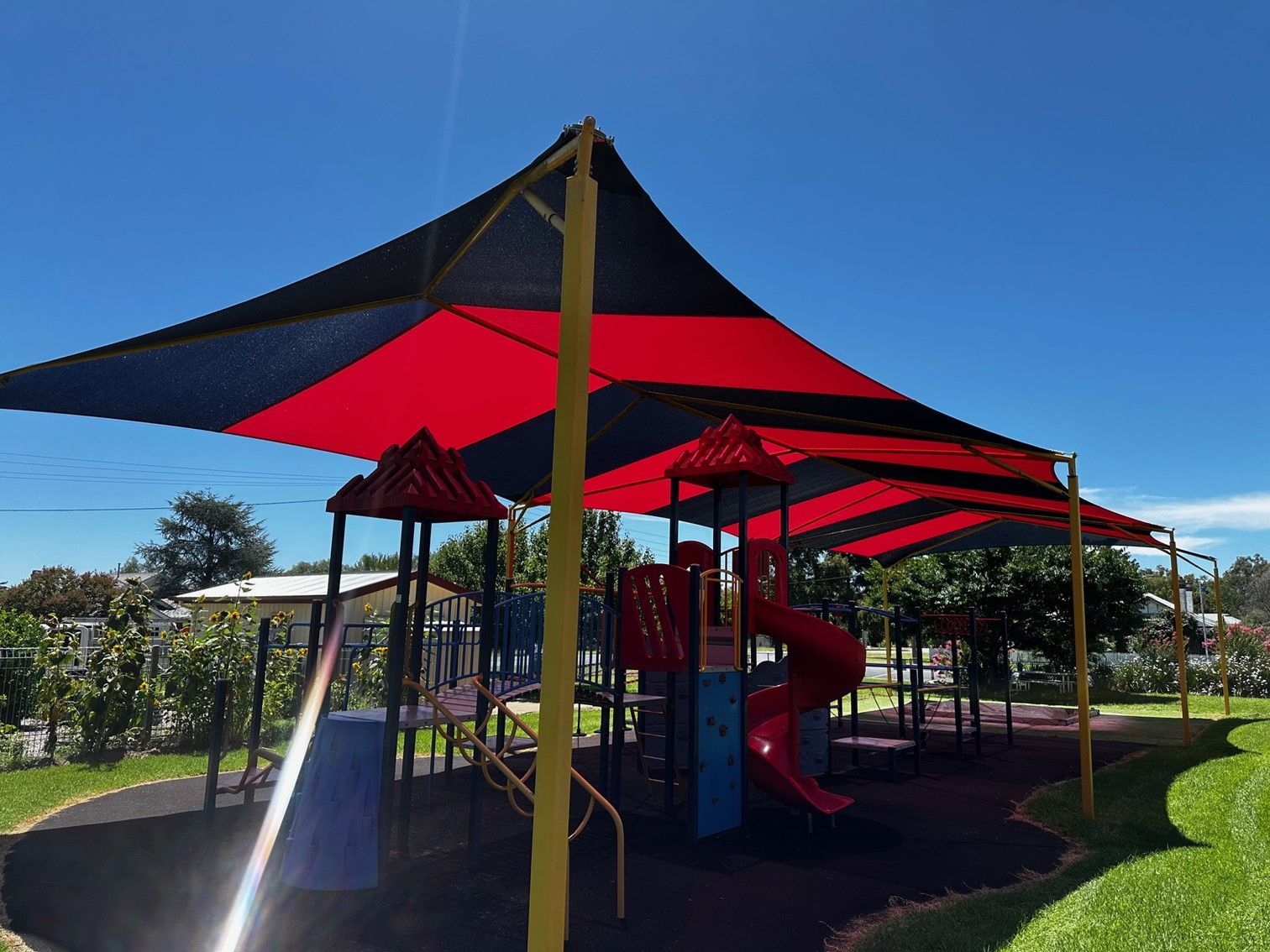 Red-and-black shade canopy over a playground with slides and climbing equipment on a sunny day — The Gazebo and Shade Centre in Bright, VIC
