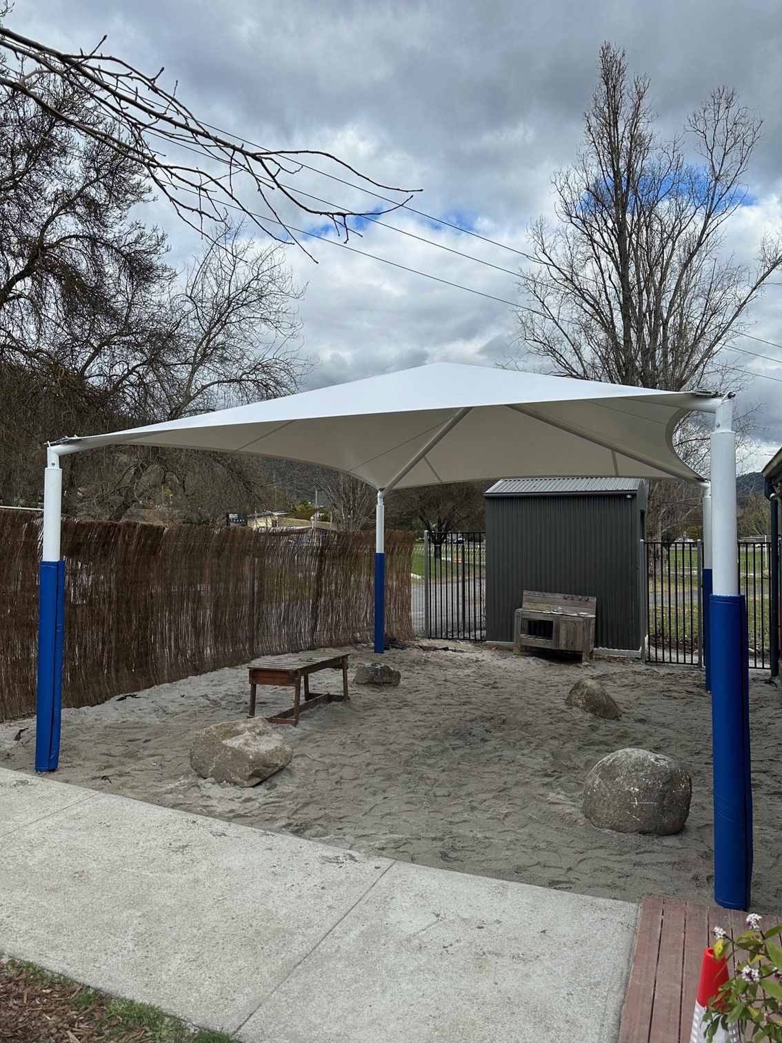 Outdoor shelter with a white canopy, blue posts, bench, and small shed on a gravel area — The Gazebo and Shade Centre in Yarrawonga, VIC