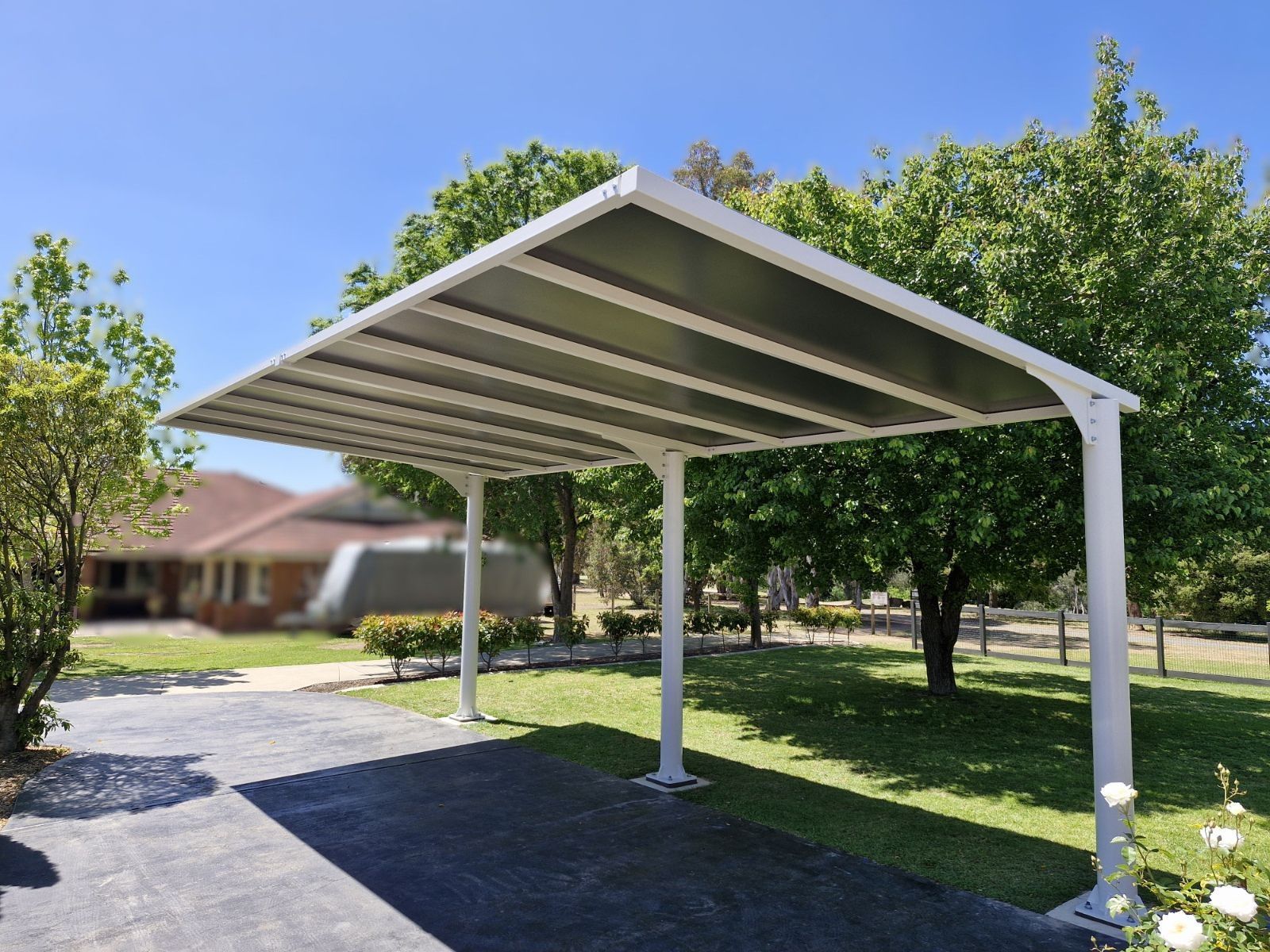 White metal carport with slanted roof in a sunny grassy yard with trees and a driveway — The Gazebo and Shade Centre in Jindera, NSW